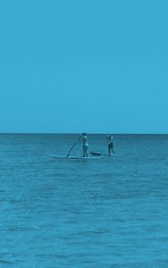Two people paddle boarding in the ocean on a clear day.