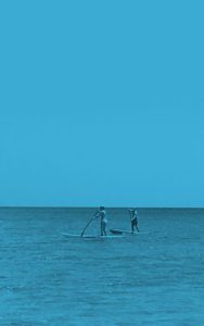 Two people paddle boarding in the ocean under a blue sky.