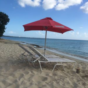 A red umbrella and two lawn chairs on the beach.