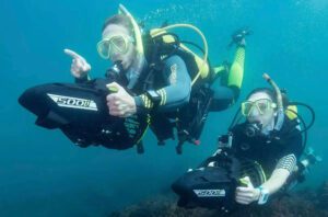 Two people in scuba gear are underwater and one is pointing.