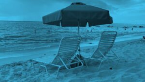 Two lawn chairs and an umbrella on the beach.