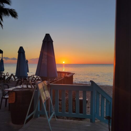 A sunset over the ocean with chairs and umbrellas.