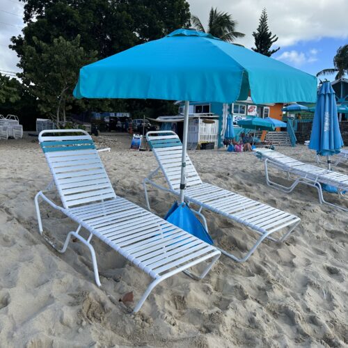 A beach with two lawn chairs and an umbrella.