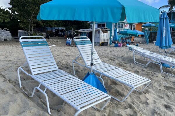 A beach with two lawn chairs and an umbrella.