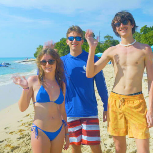 Three people standing on the beach in their swim trunks